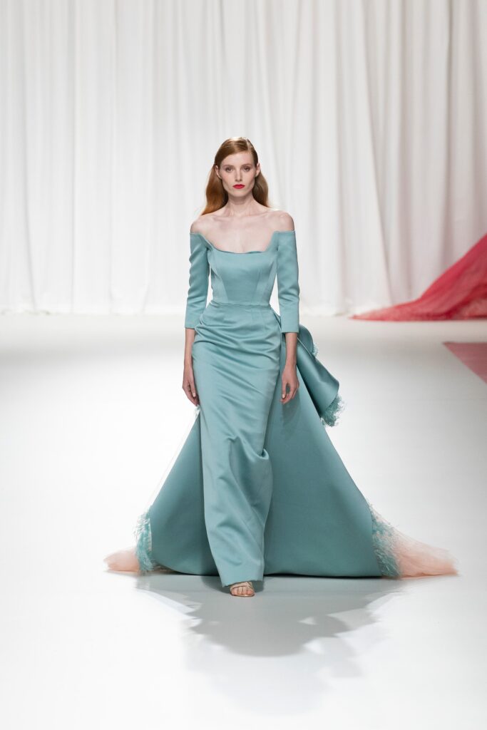 A fitted blue silk gown with long sleeves and an off-shoulder design featuring a tiered detail.