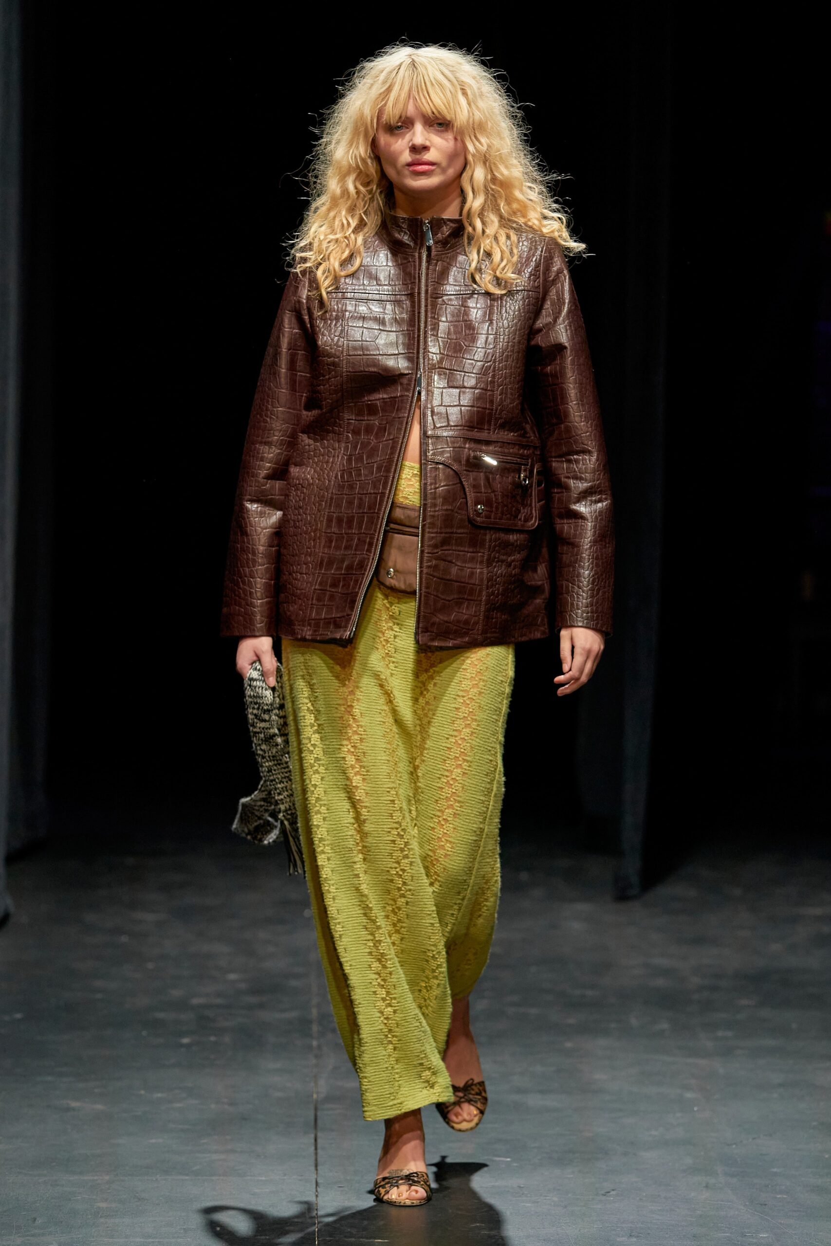 A relaxed brown leather jacket layered over a green dress with a V-neckline.
