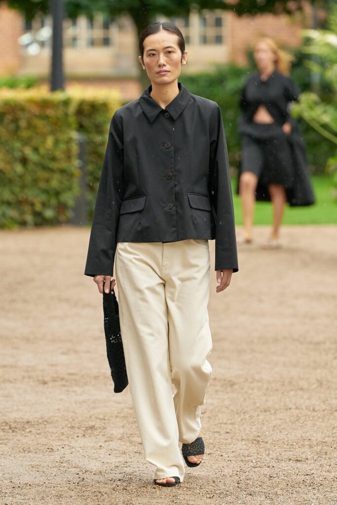 A relaxed black cotton jacket with long sleeves and a collared neckline paired with straight-leg beige pants.