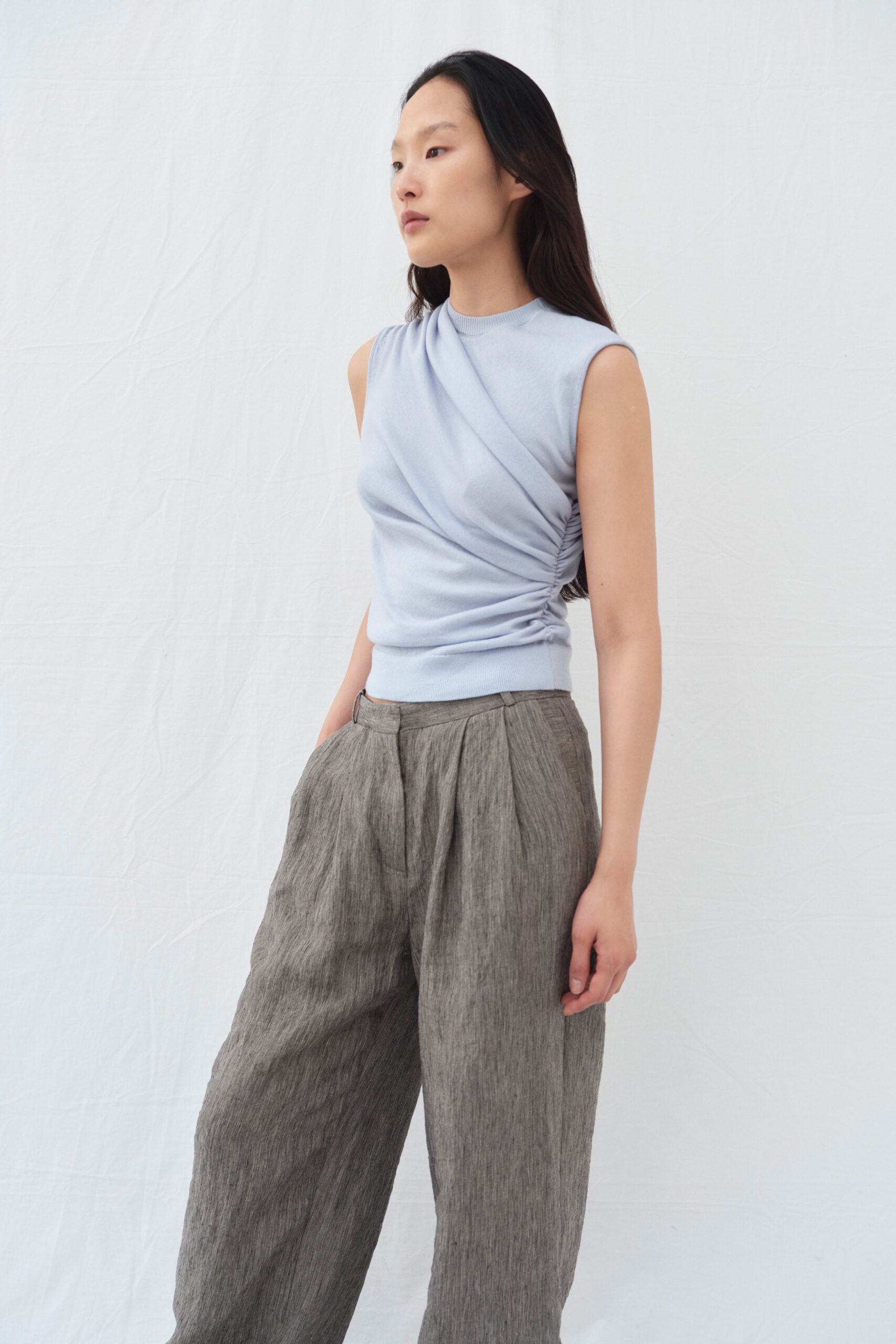 A relaxed light blue sleeveless top paired with wide-leg gray pants featuring a draped design.