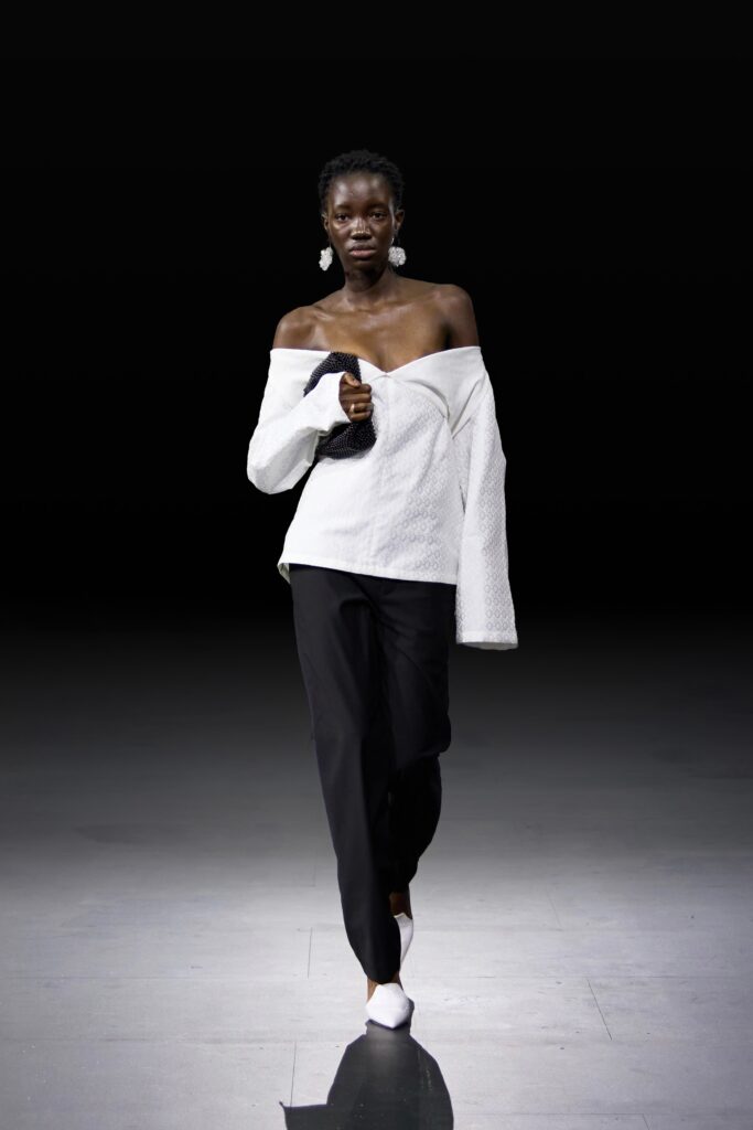 An oversized white off-shoulder top paired with relaxed black pants for a chic look.