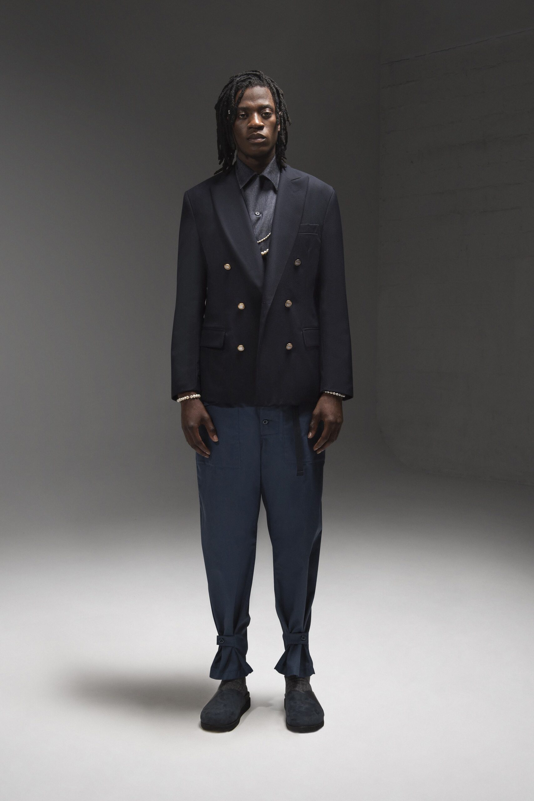 A fitted black blazer with long sleeves and a collared neckline, paired with tailored blue pants.