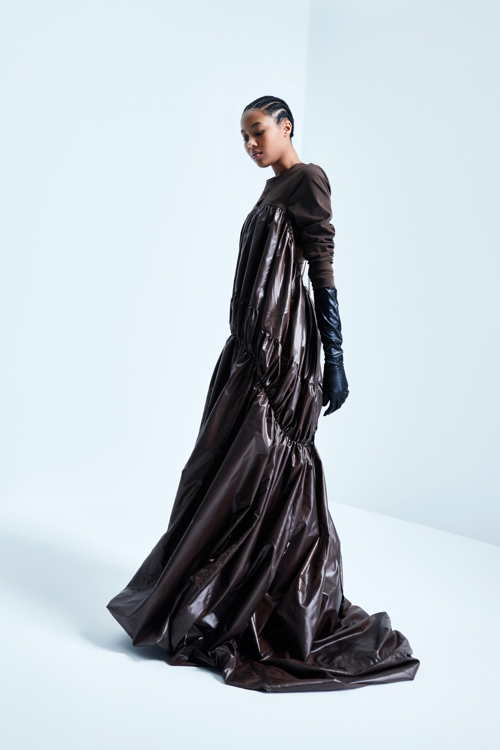 This relaxed dress features a dramatic silhouette crafted from brown leather, with a high neckline and long sleeves that flow gracefully. The draped design creates an intriguing interplay of volume and texture, enhancing the overall visual impact.