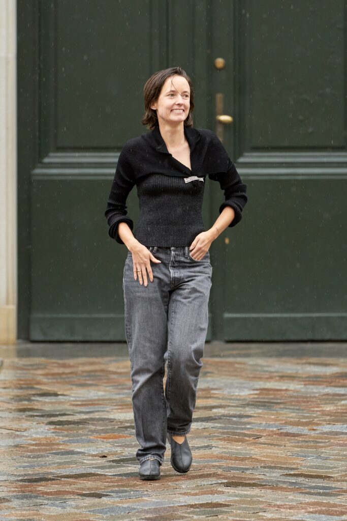 A fitted black long-sleeve top with a collar paired with straight-leg gray pants.