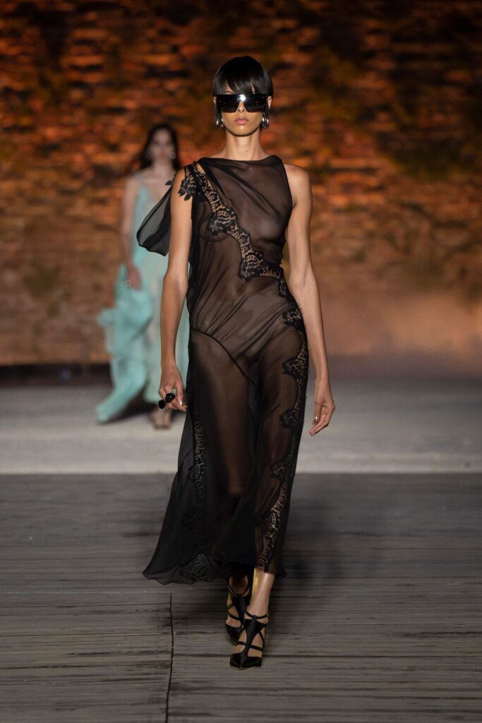 A fitted black sheer dress with a V-neckline and asymmetric design detail.
