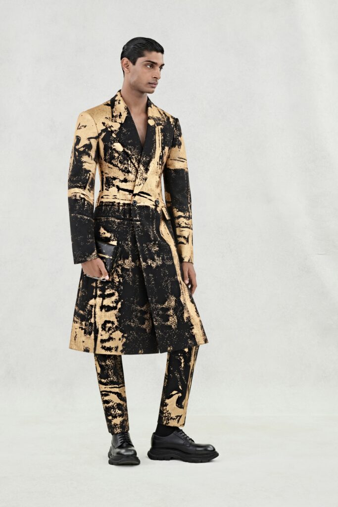 A fitted black and gold printed coat paired with matching pants, featuring an asymmetric design.