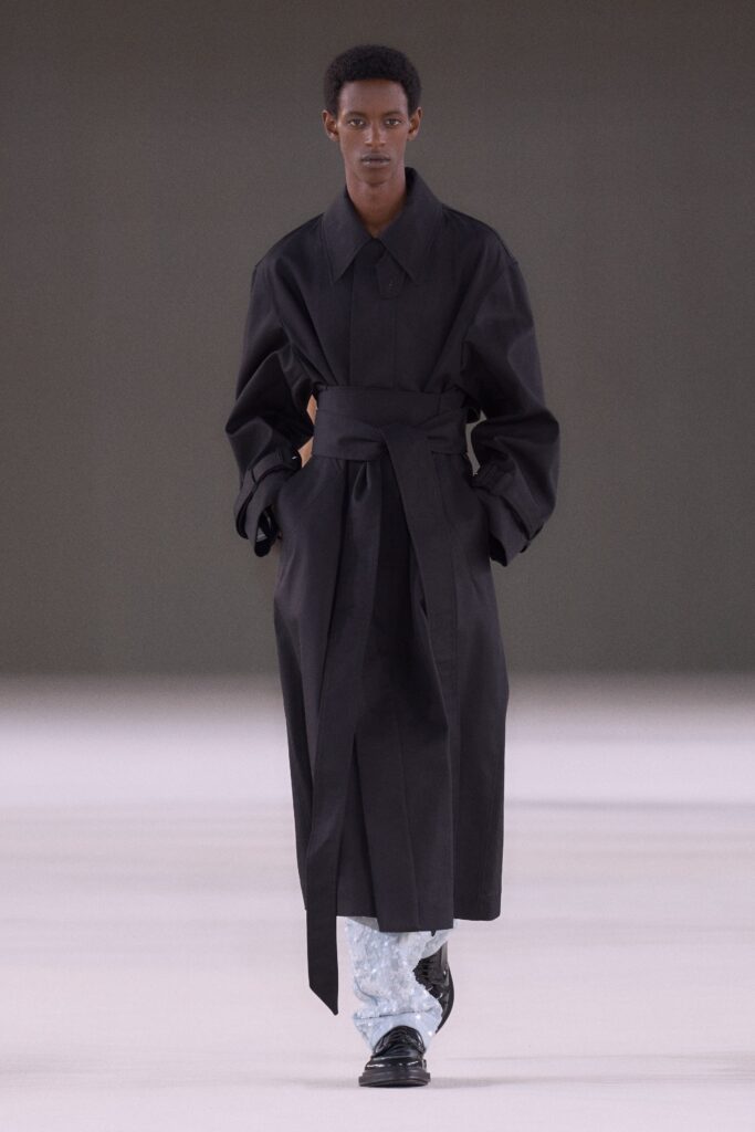 A relaxed black cotton coat with long sleeves and a belted design.