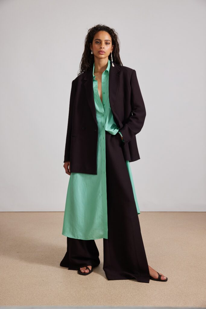 A relaxed black jacket layered over a green collared dress with button details.