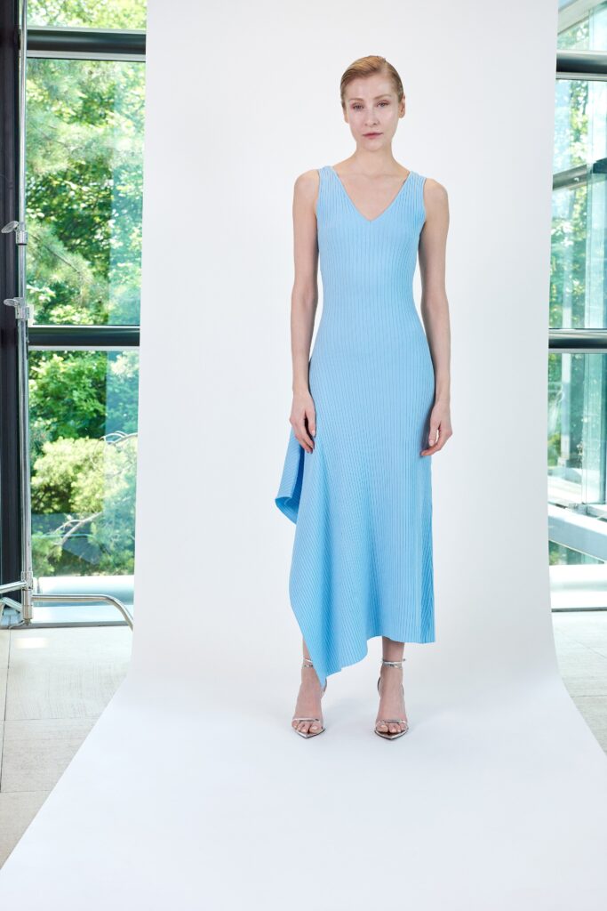 A fitted blue sleeveless dress with a V-neckline and asymmetric hem.