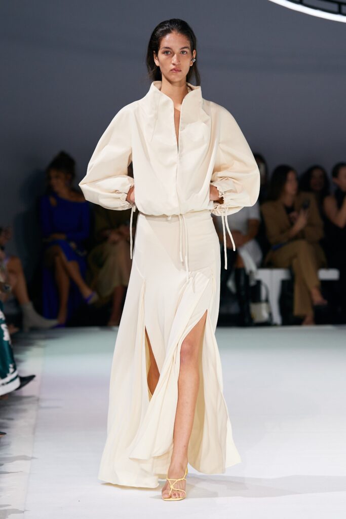A fitted cream silk dress with long sleeves, a high neckline, and a stylish slit.