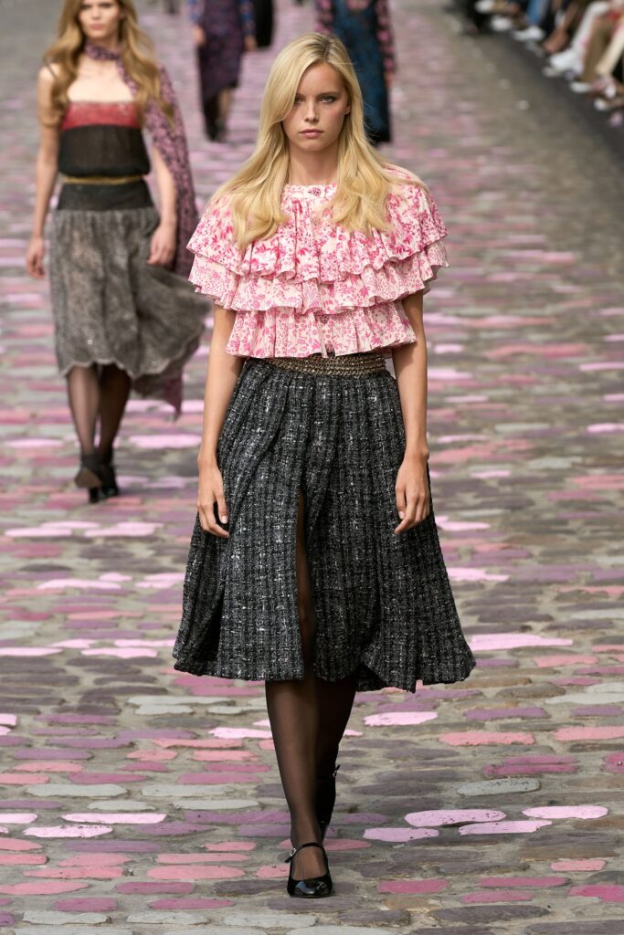 A fitted pink ruffled top paired with a high-waisted black pleated skirt.