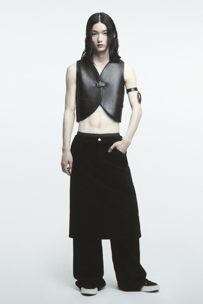 A fitted black leather sleeveless vest paired with high-waisted black pants featuring an asymmetric design.