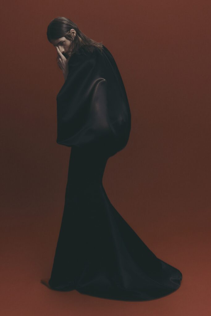 A fitted black silk sleeveless dress with a high neckline and flared silhouette.