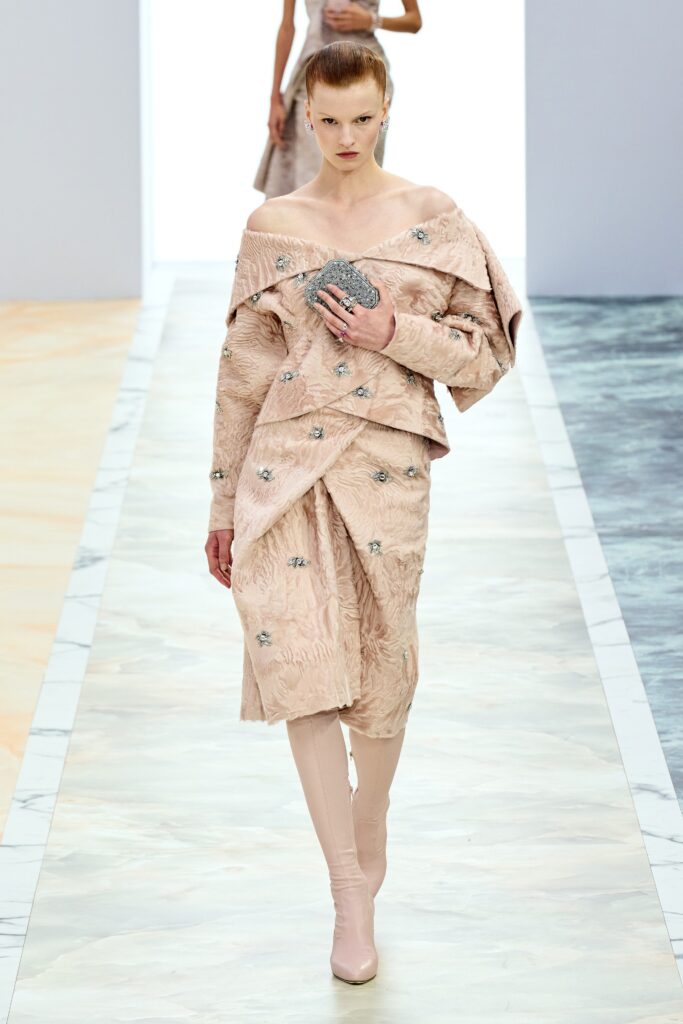 A fitted pink silk dress with long sleeves and an off-shoulder design featuring layered and embroidered details.