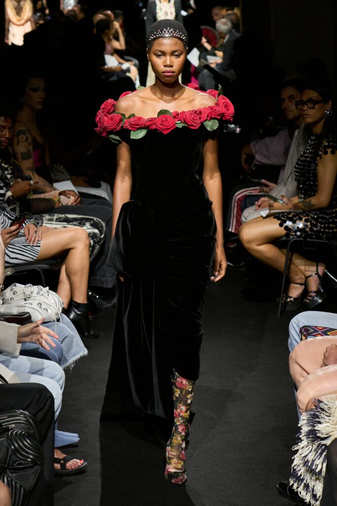 A fitted black velvet dress with an off-shoulder design and flared silhouette adorned with roses.