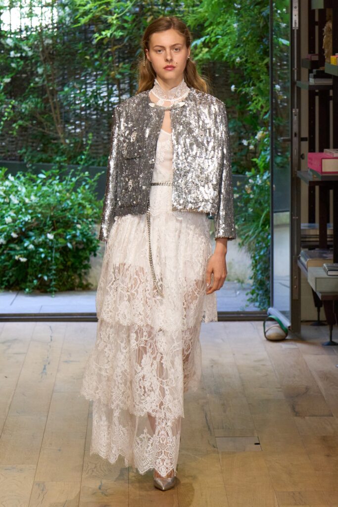 A fitted white lace dress layered with a sequined long-sleeve jacket, creating an elegant look.
