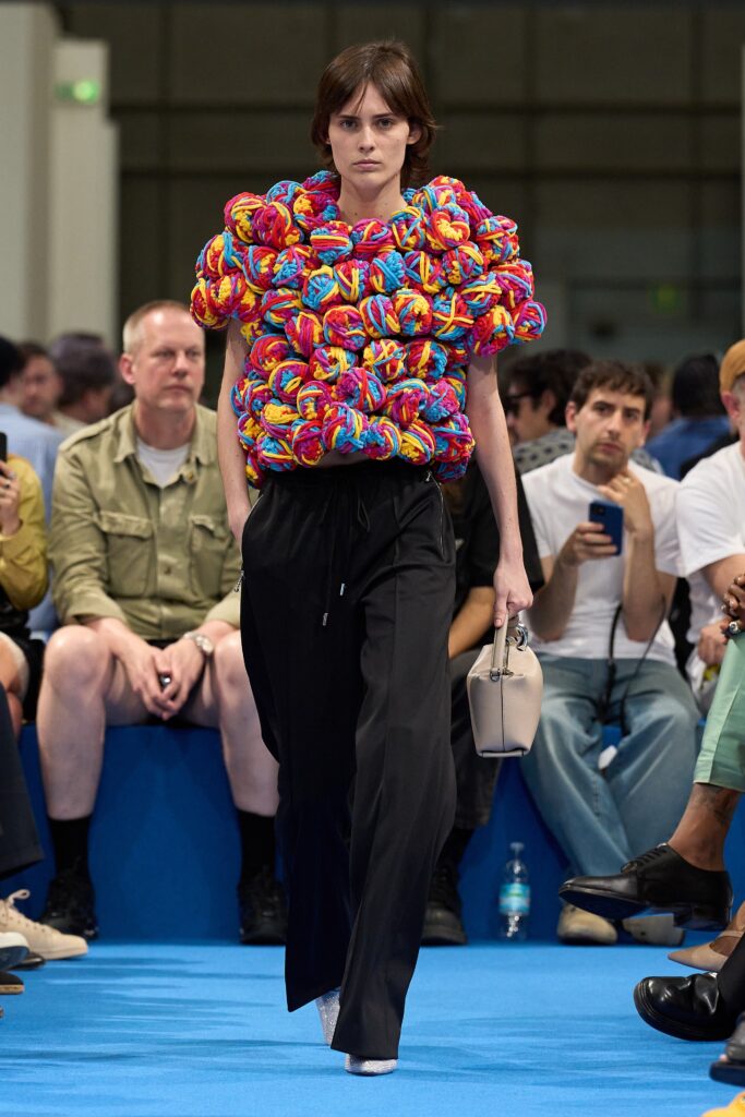 A relaxed multicolor top paired with black pants, featuring a high-neck and layered design.