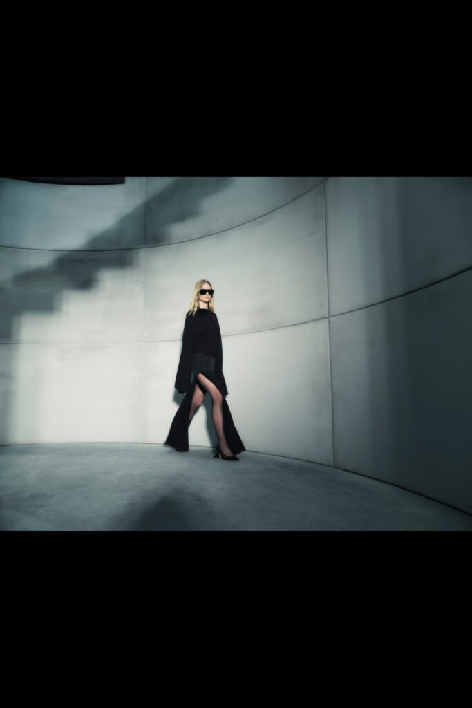 A fitted black silk dress with a V-neckline and a high slit detail.