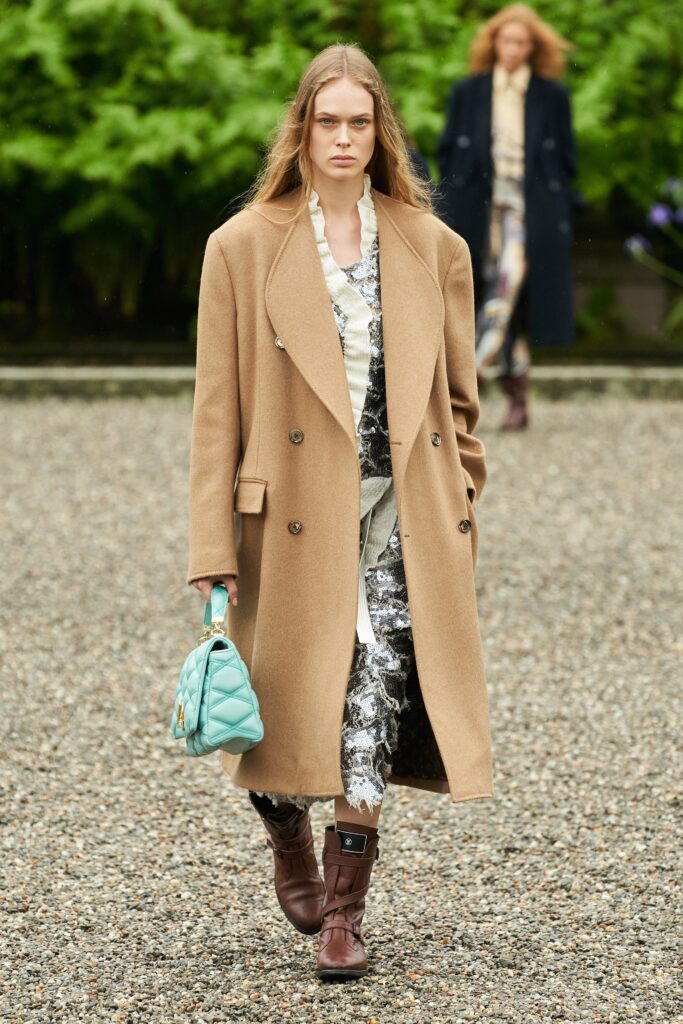 A fitted brown wool coat layered over a white silk dress with a collared neckline.