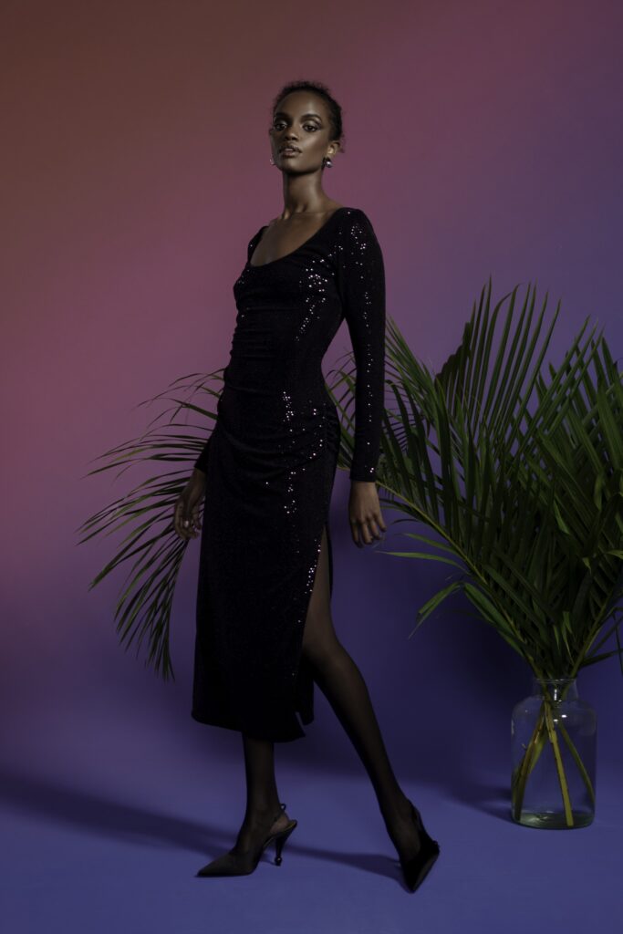 A fitted black silk dress with long sleeves, a V-neckline, and a stylish slit.