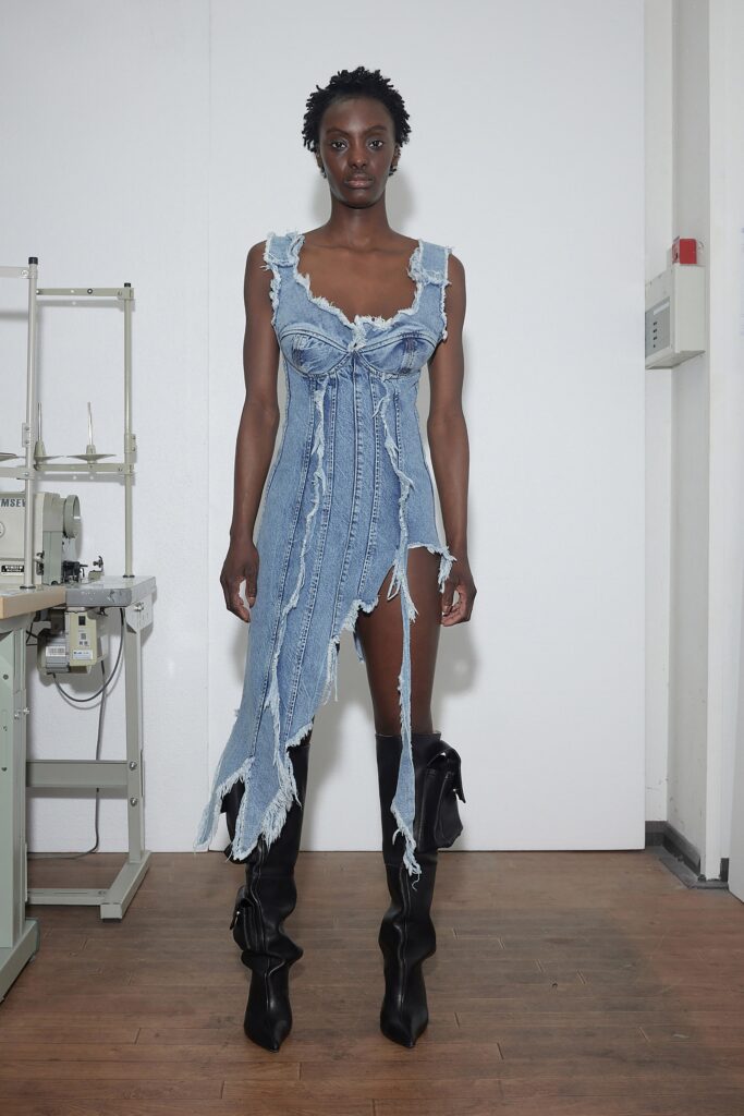 A fitted blue denim dress with a V-neckline and asymmetric fringed detail.