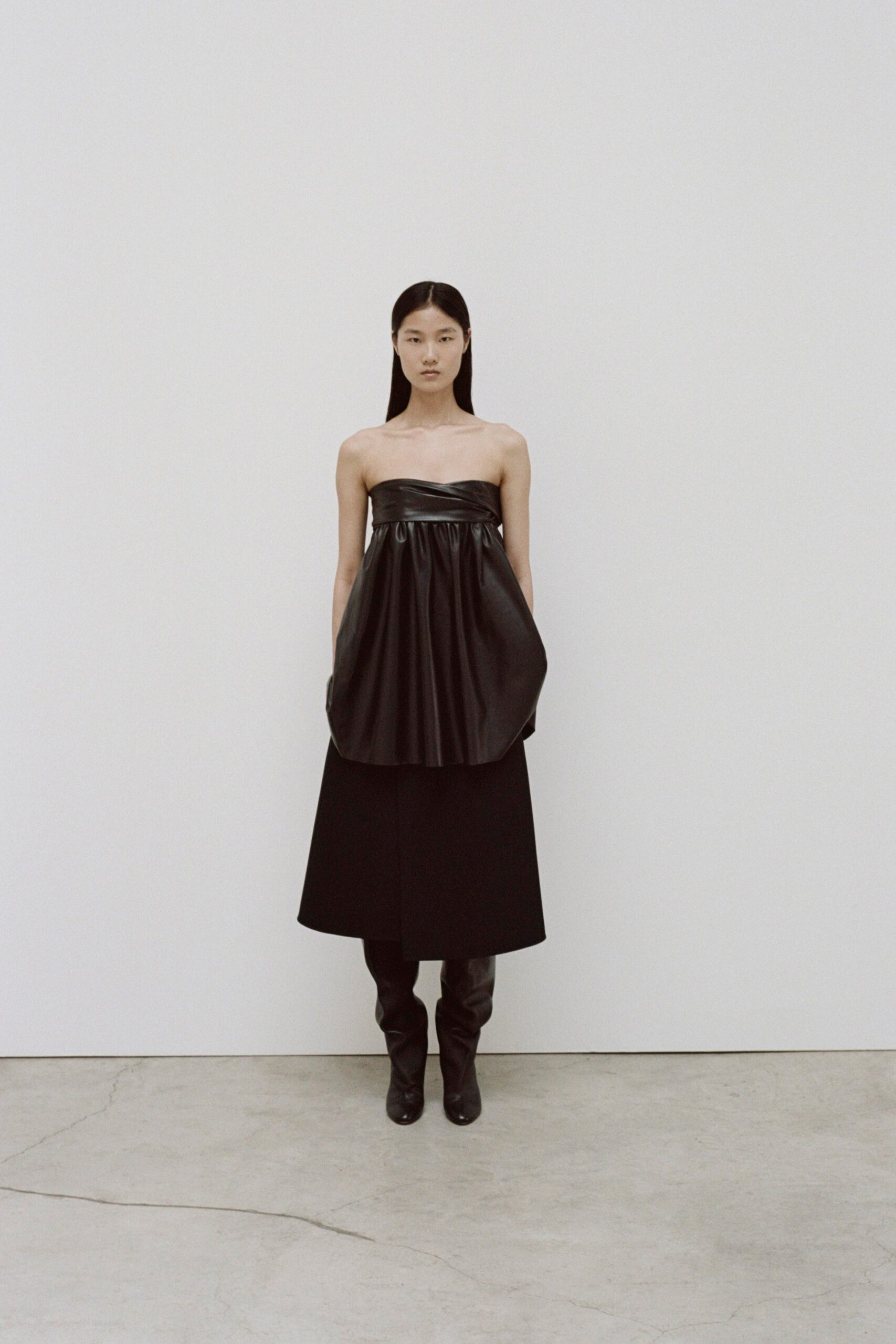 A fitted black leather sleeveless dress with a V-neckline and asymmetric design.