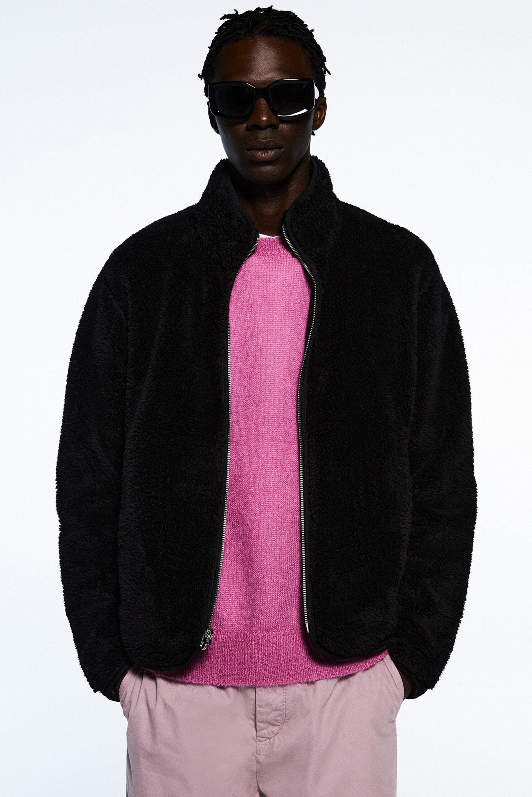 A relaxed black faux-fur jacket paired with a long-sleeve pink sweater featuring a zippered front.