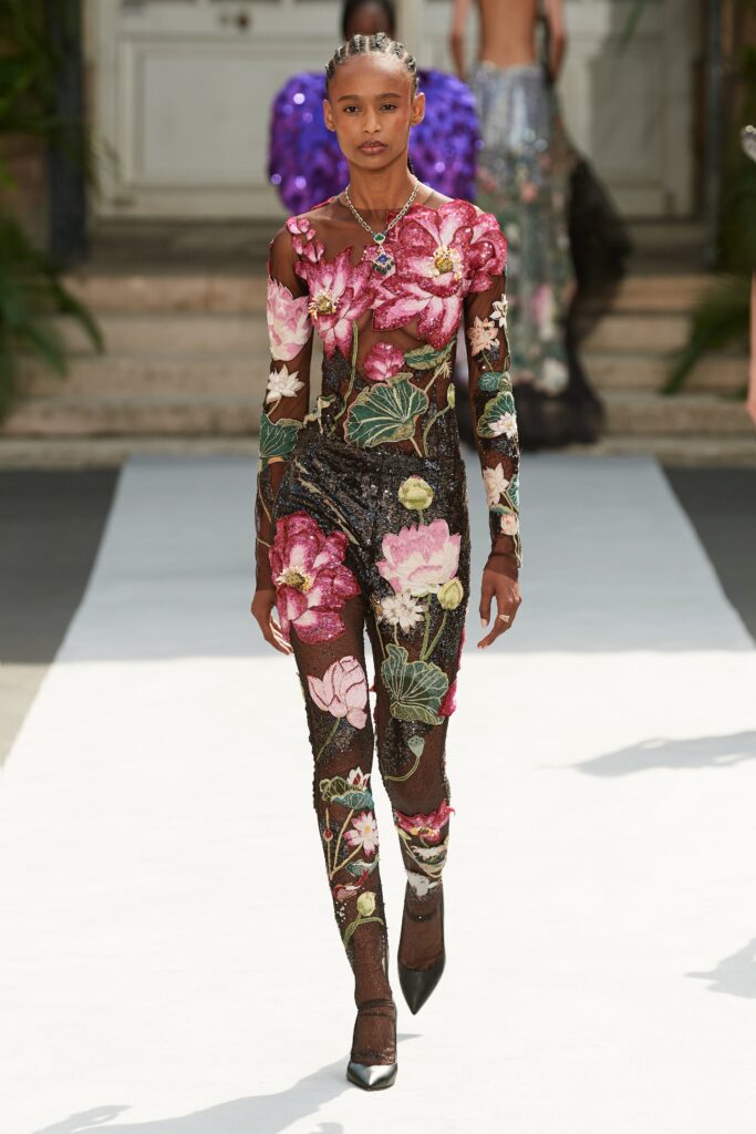 A fitted black mesh jumpsuit with long sleeves, a V-neckline, and floral sequined details.