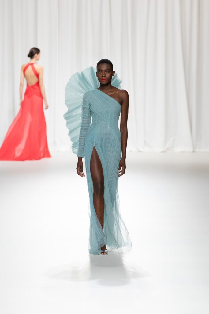 A fitted blue silk sleeveless dress with a high neckline and asymmetric design featuring a slit.