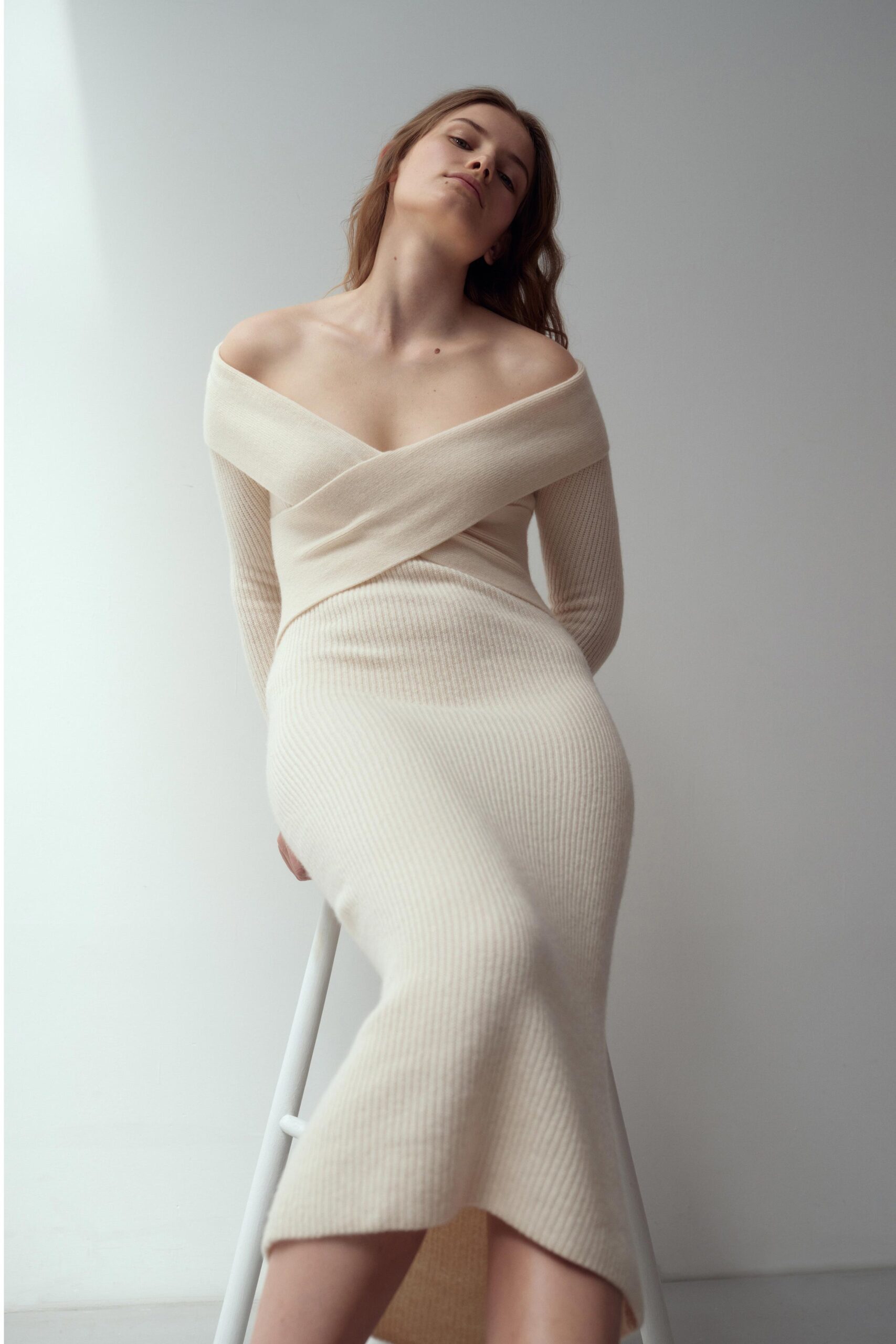 A fitted beige knit dress with a V-neckline and a slit detail.