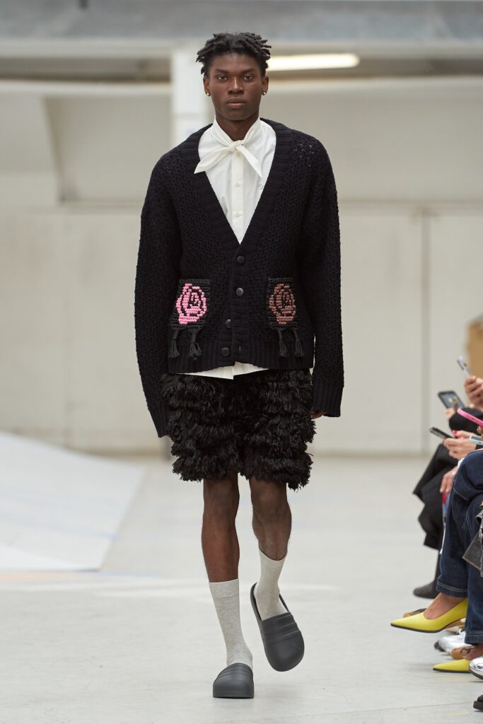 A relaxed black knitted cardigan with long sleeves paired with fringed black shorts.