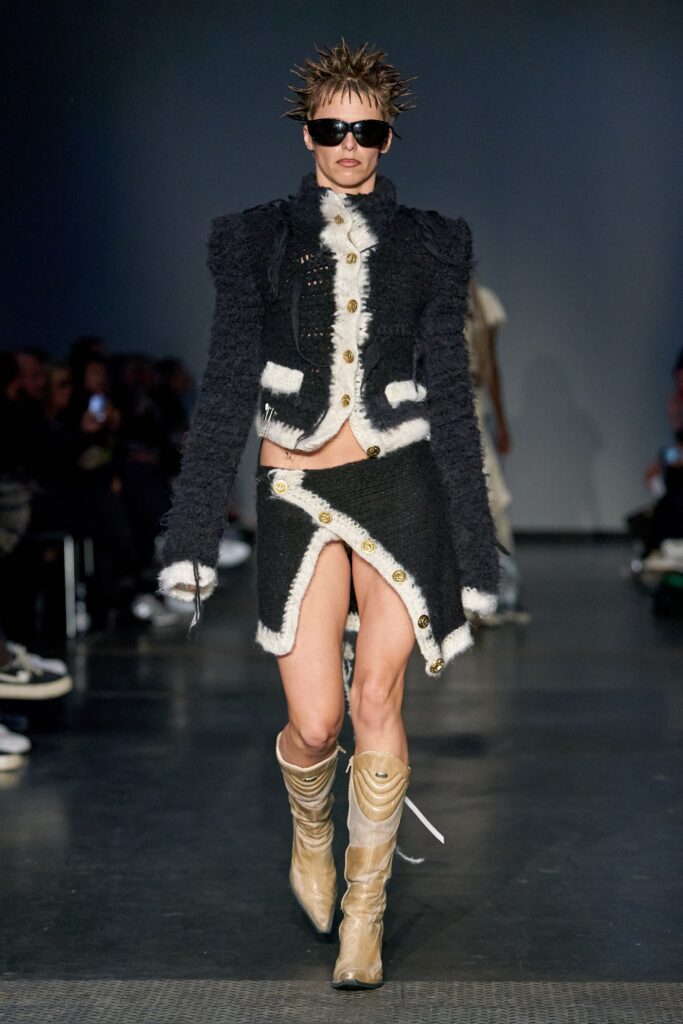 A fitted black wool jacket with long sleeves and a collared design, paired with an asymmetric skirt.