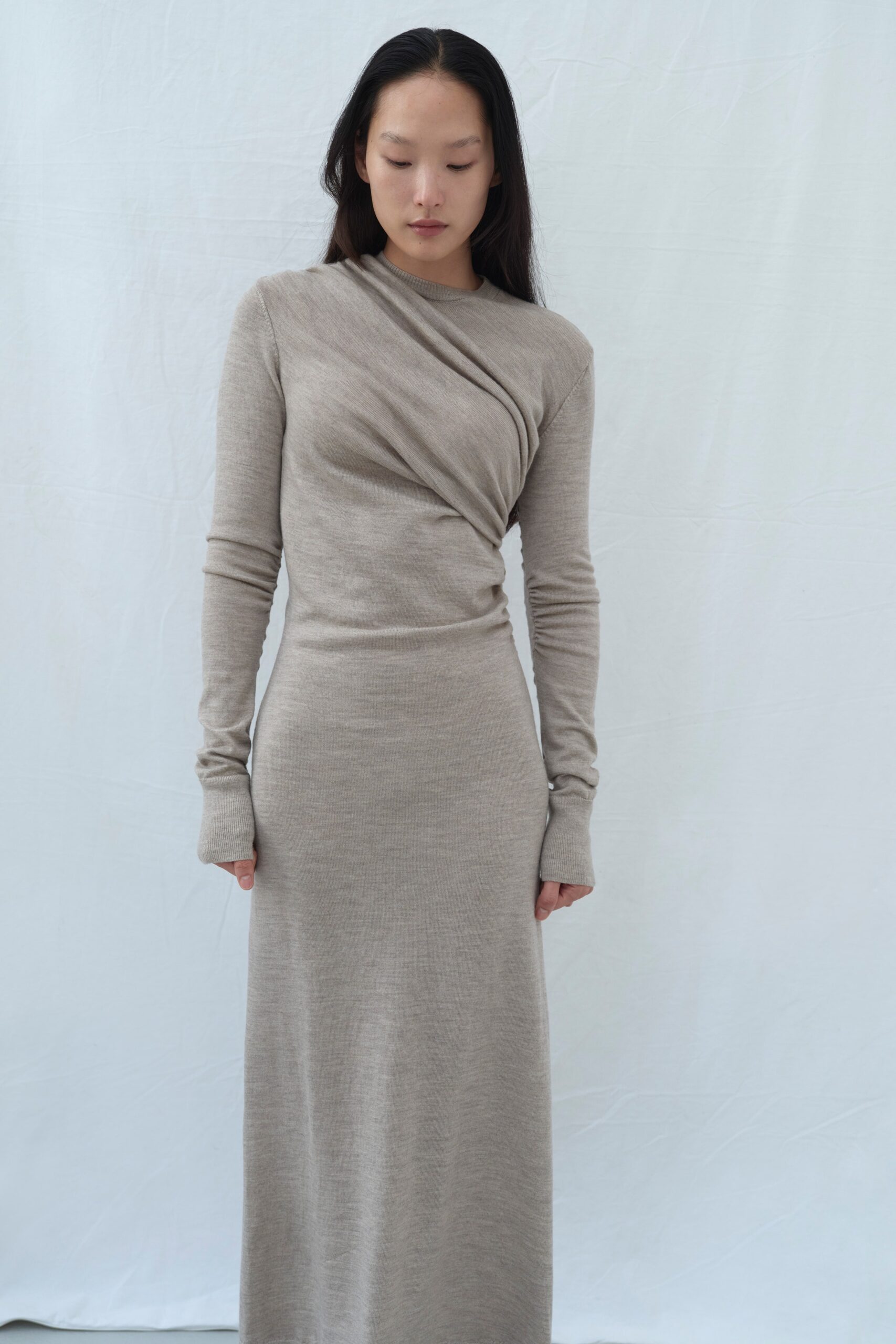A fitted beige wool dress with long sleeves and a draped design.