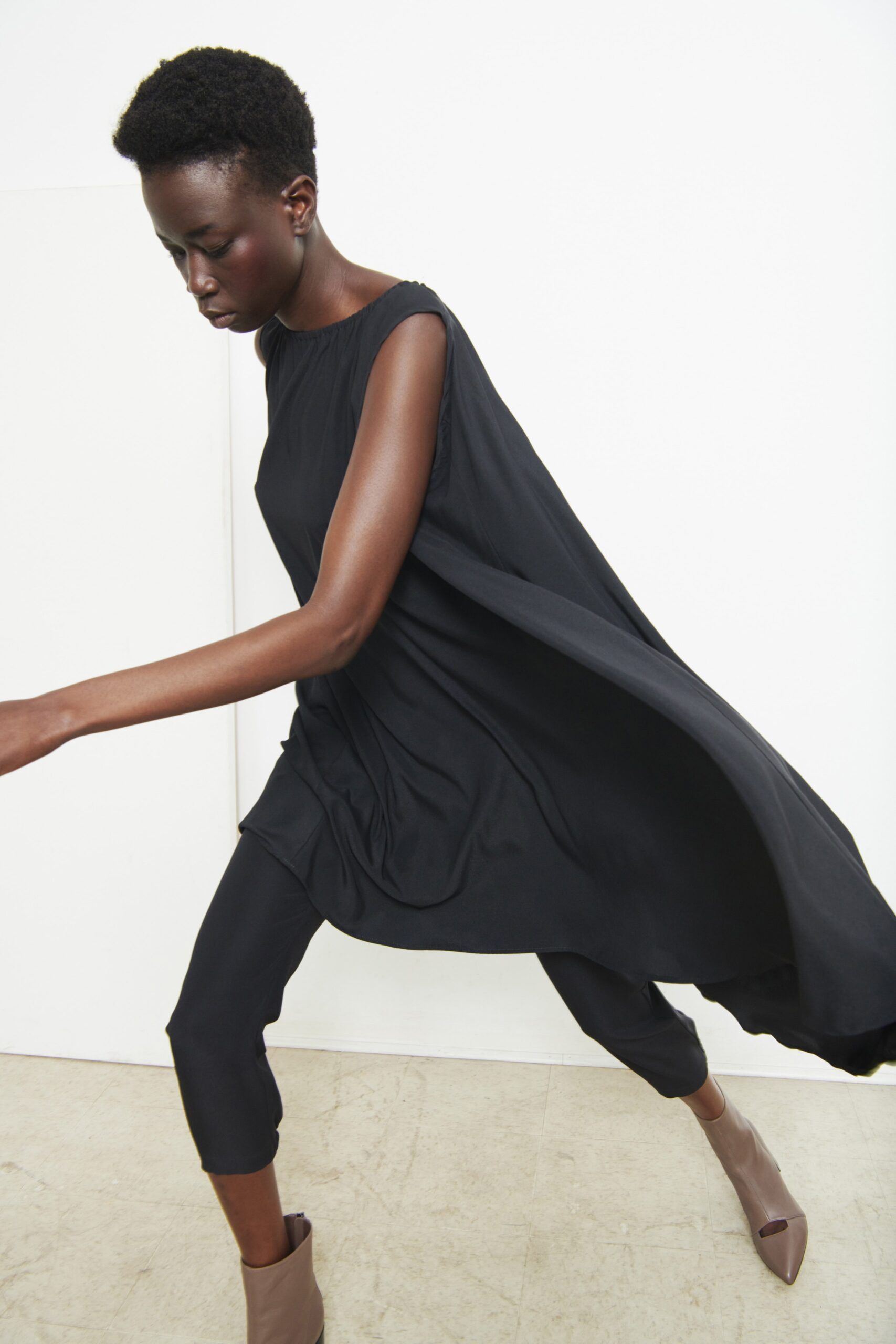 A relaxed black sleeveless dress with an asymmetric design, paired with fitted pants.