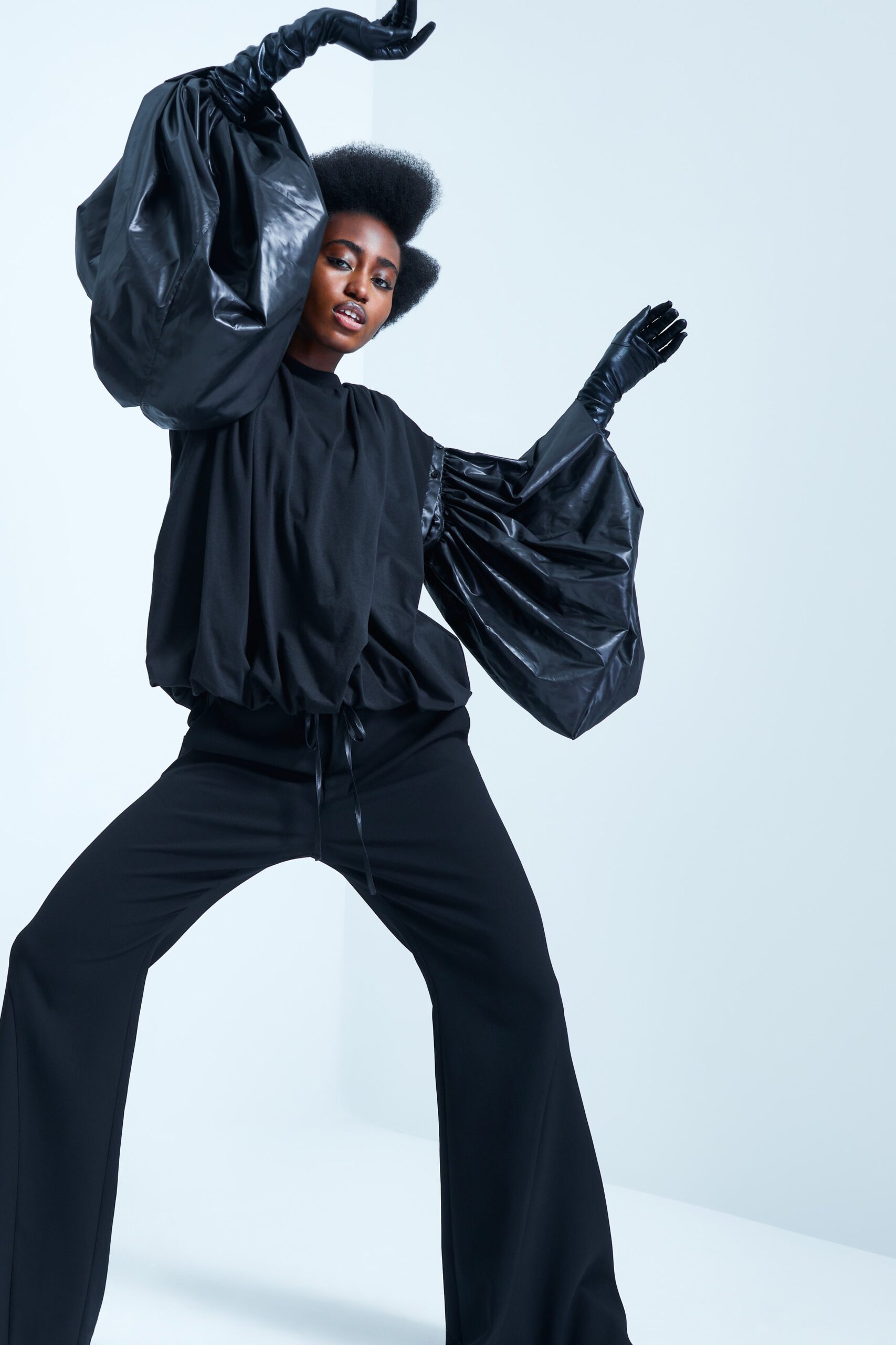 This ensemble features a relaxed black top with voluminous sleeves that create a striking silhouette, paired with wide-leg pants that enhance the fluidity of movement. The combination of cotton and leather adds a textural contrast, while the pleated details introduce a dynamic element to the overall look.
