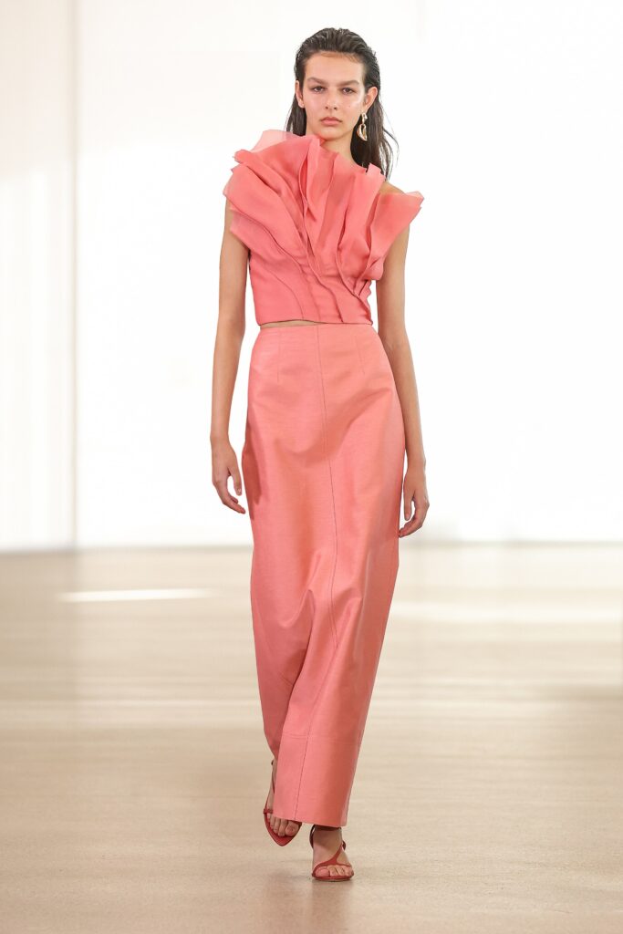 A fitted pink silk sleeveless top with ruffles paired with a straight-leg skirt.