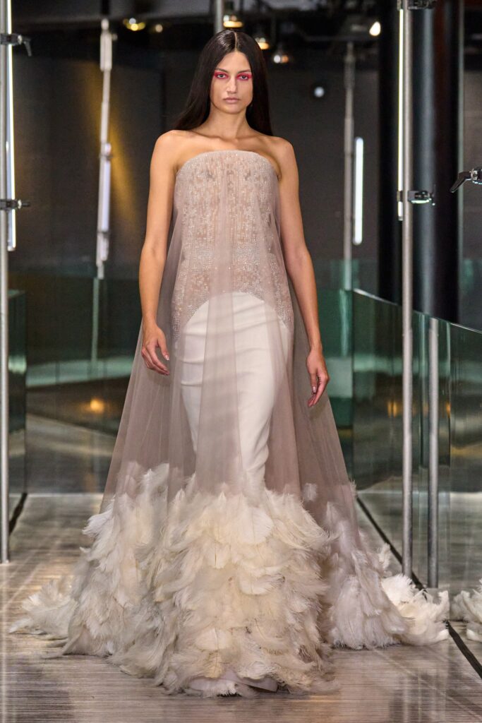 A fitted beige silk gown with a strapless design and tiered feather detailing at the hem.