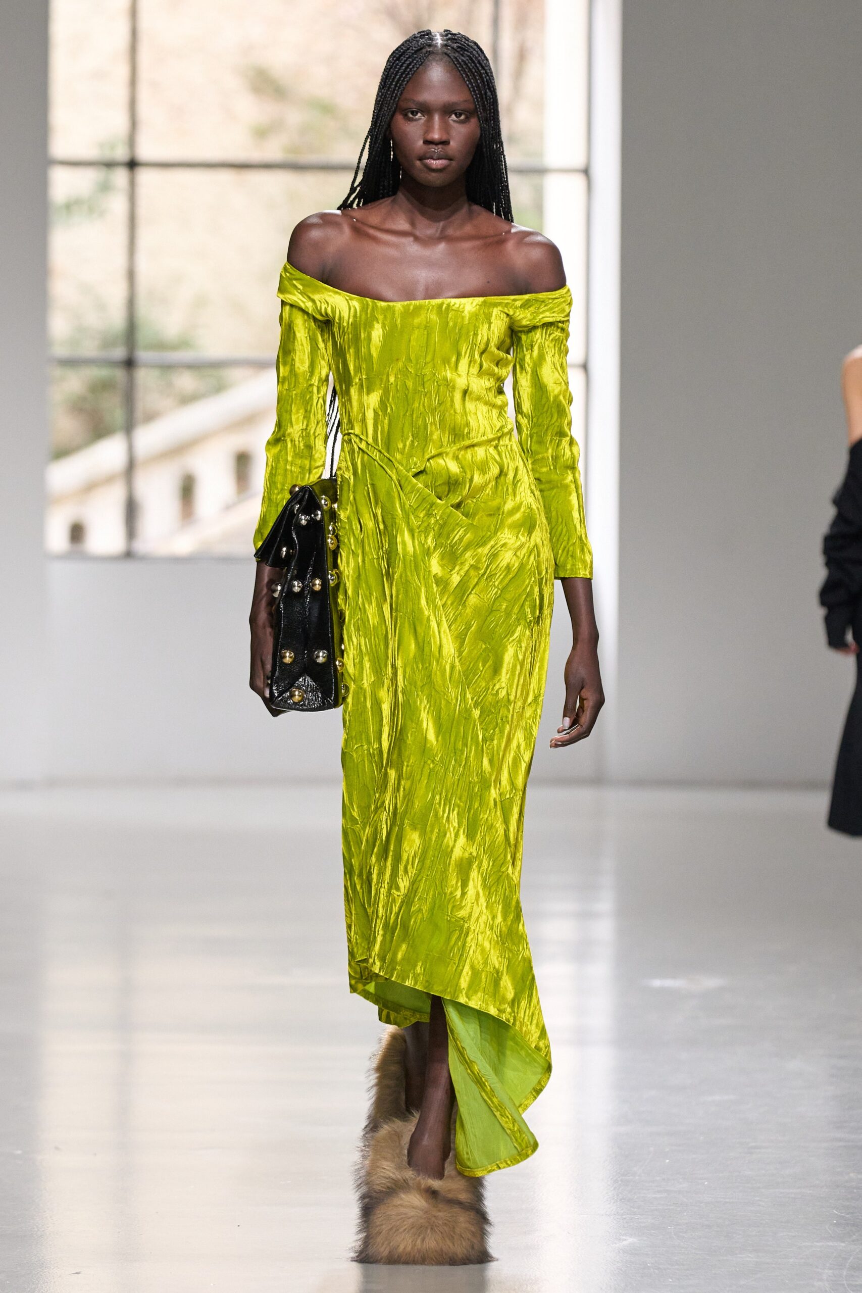 A fitted green silk dress with long sleeves and an off-shoulder design featuring an asymmetric hem.