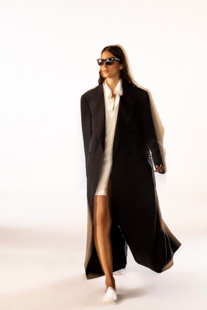 A fitted black coat layered over a white dress with a collared neckline and asymmetric design.