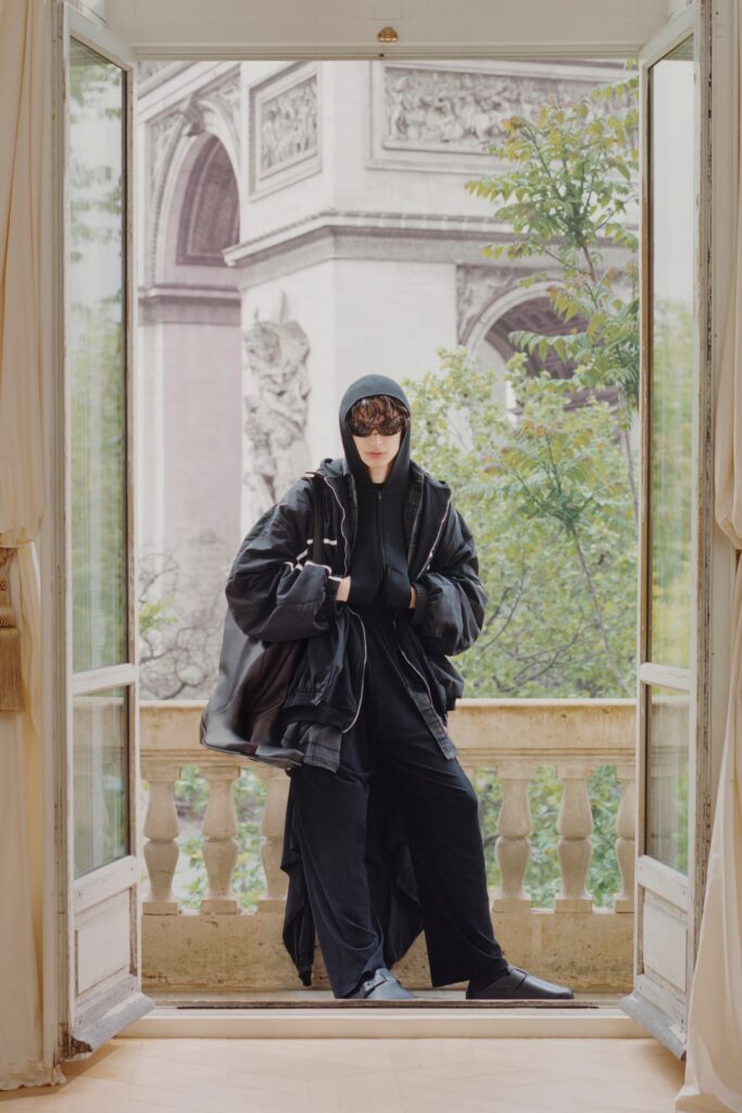 A relaxed black coat with a hood, paired with matching black pants, creating a layered look.