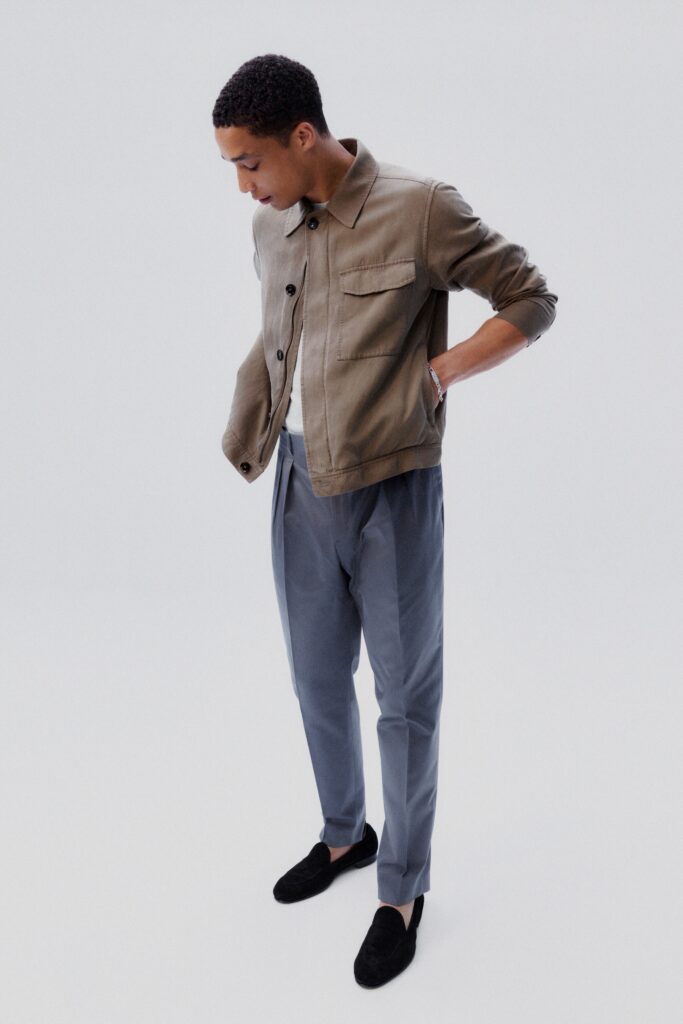 A relaxed beige cotton jacket with a collared neckline, paired with pleated gray pants.