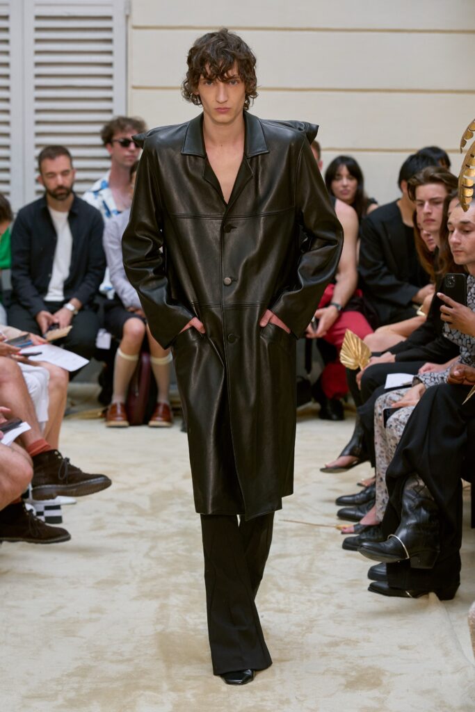 A fitted black leather coat with long sleeves and a collared design, paired with straight-leg pants.