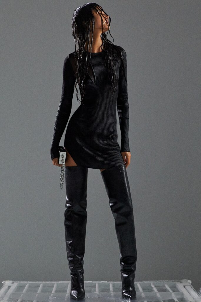 A fitted black dress with long sleeves, a high neckline, and a stylish slit.