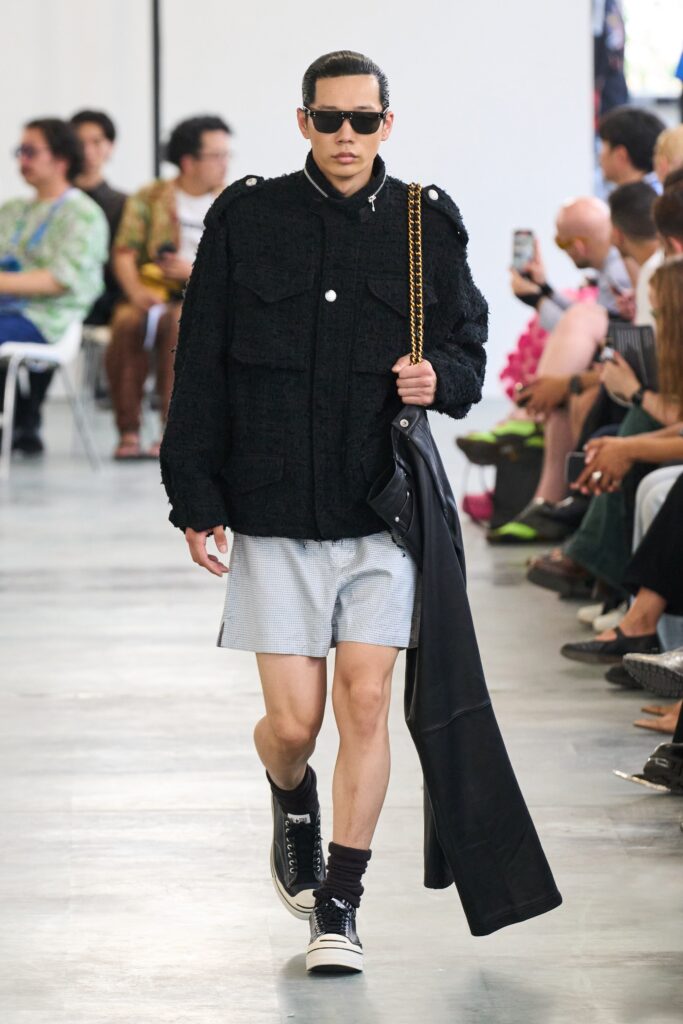 A relaxed black jacket with long sleeves and collared design paired with gray shorts.