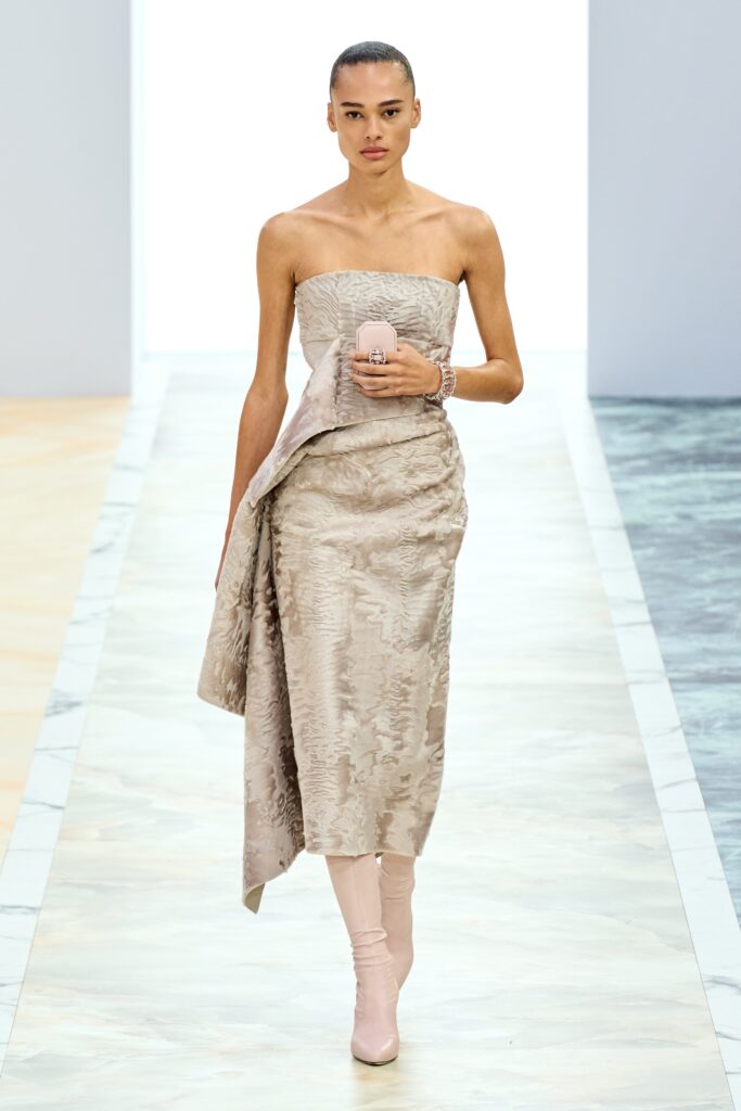 A fitted beige silk strapless dress with an asymmetric design detail.