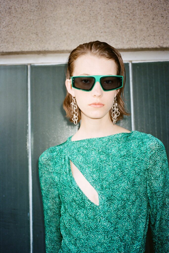 A fitted green dress with long sleeves and an asymmetric cutout detail.