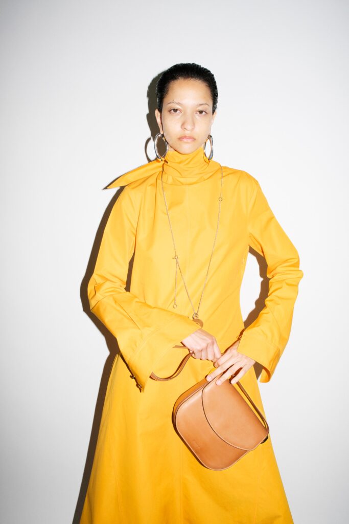 A fitted yellow cotton dress with long sleeves and a high-neck design featuring an asymmetric detail.