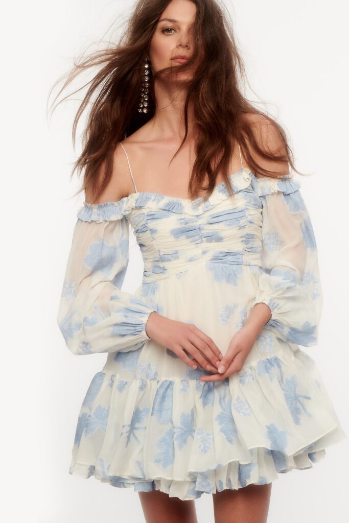 A fitted white and blue dress with long sleeves and an off-shoulder design featuring ruffled details.