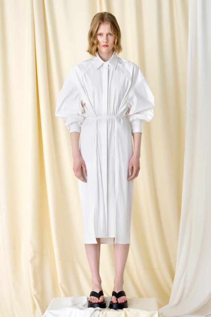 A fitted white dress with pleated details, long sleeves, and a collared neckline.