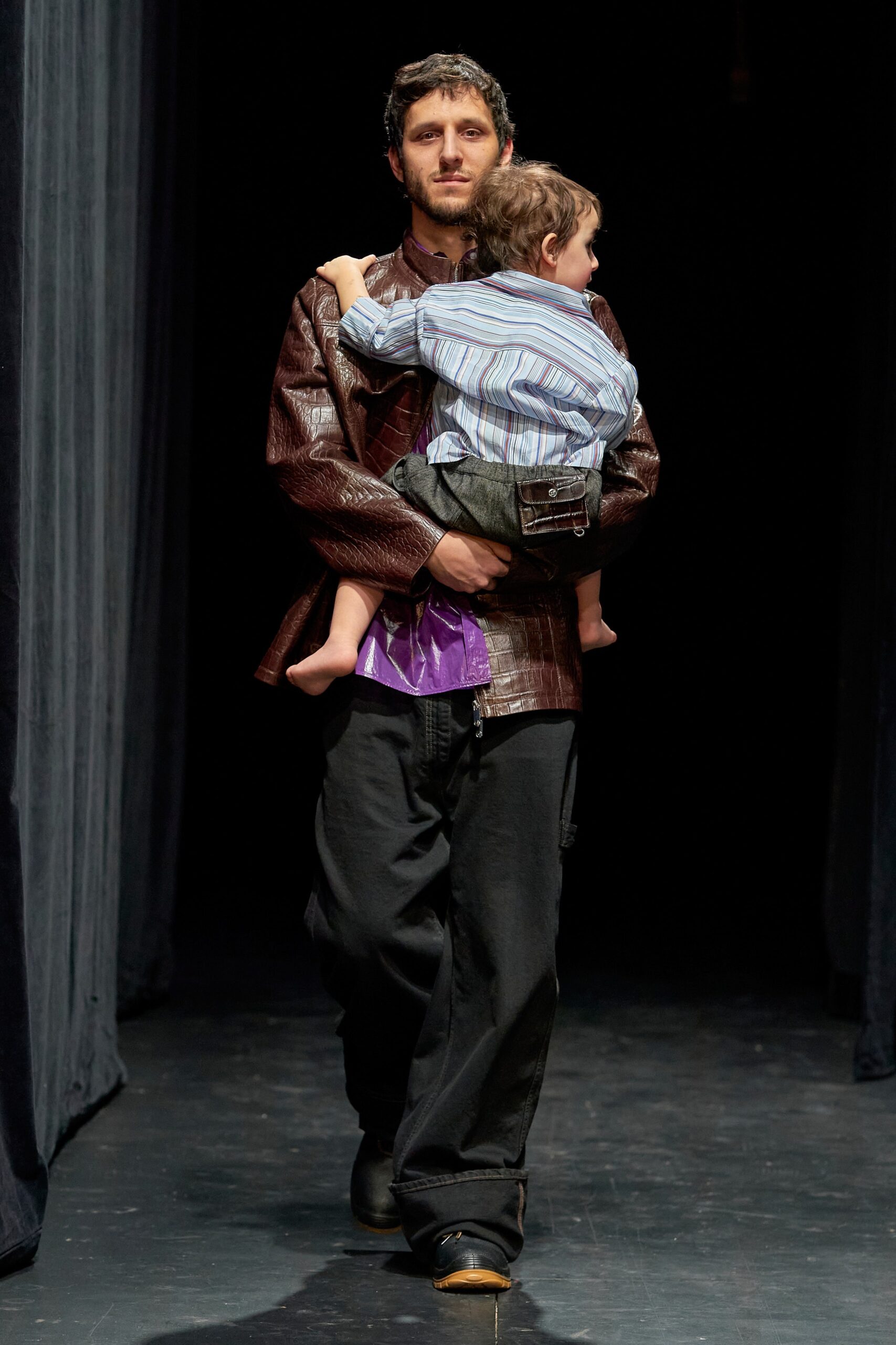 A relaxed brown leather jacket with long sleeves and black cotton pants.